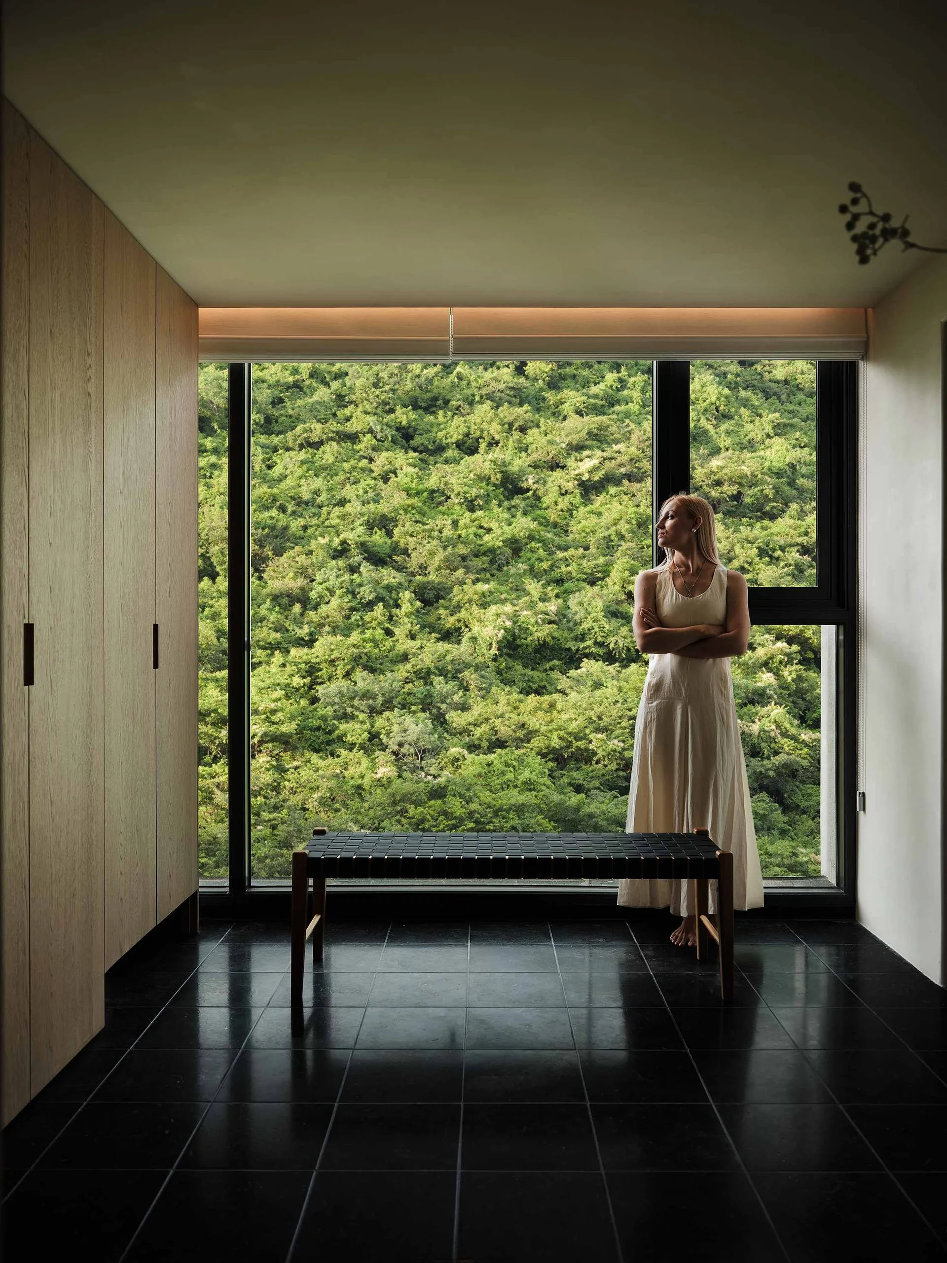 现代极简卧室实景:左侧高柜与墙面一体,木纹门板配黑色竖向拉手,窗边长凳呼应整体调性
